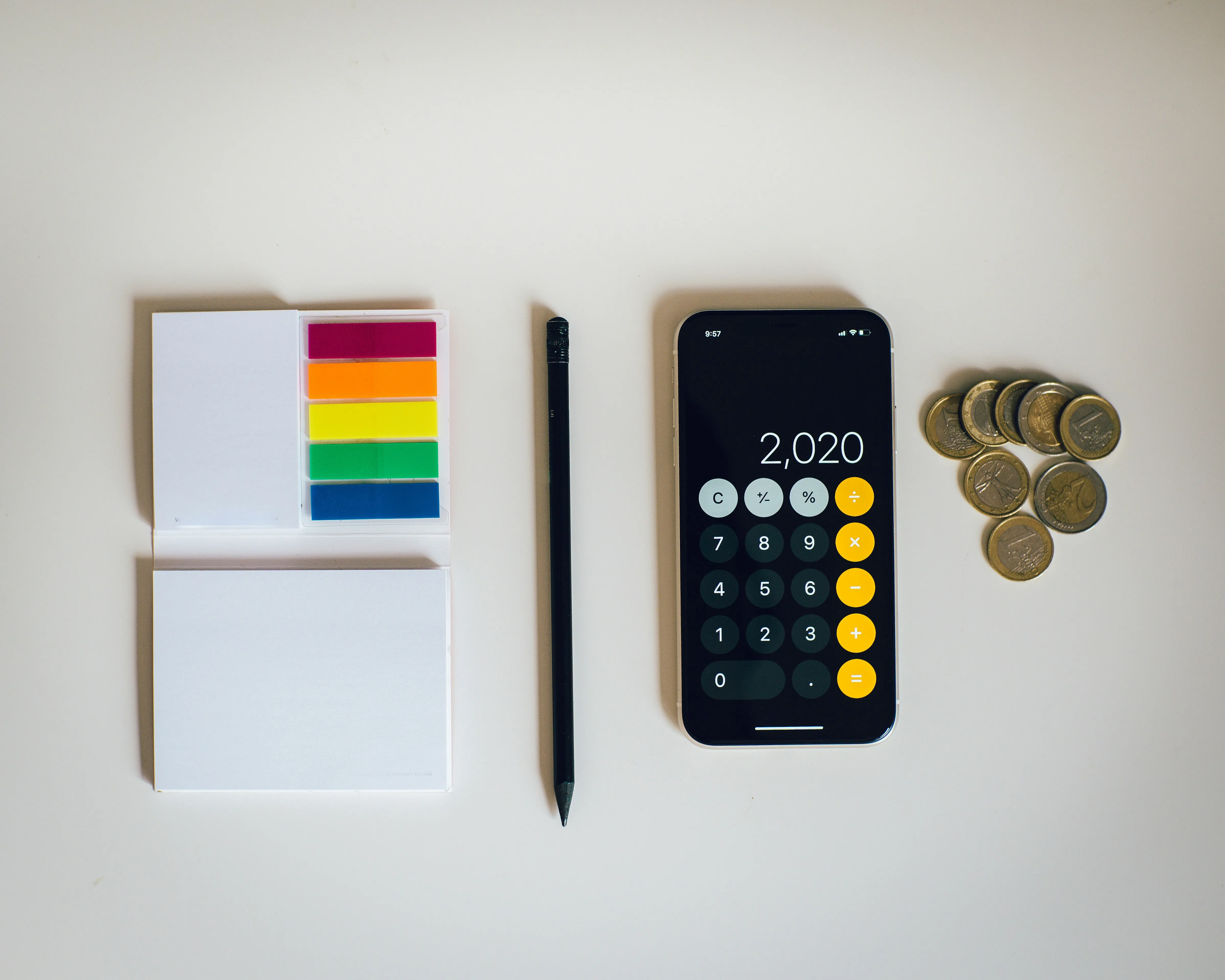 Office desk with sticky notes, pencil, smartphone calculator, and coins.​