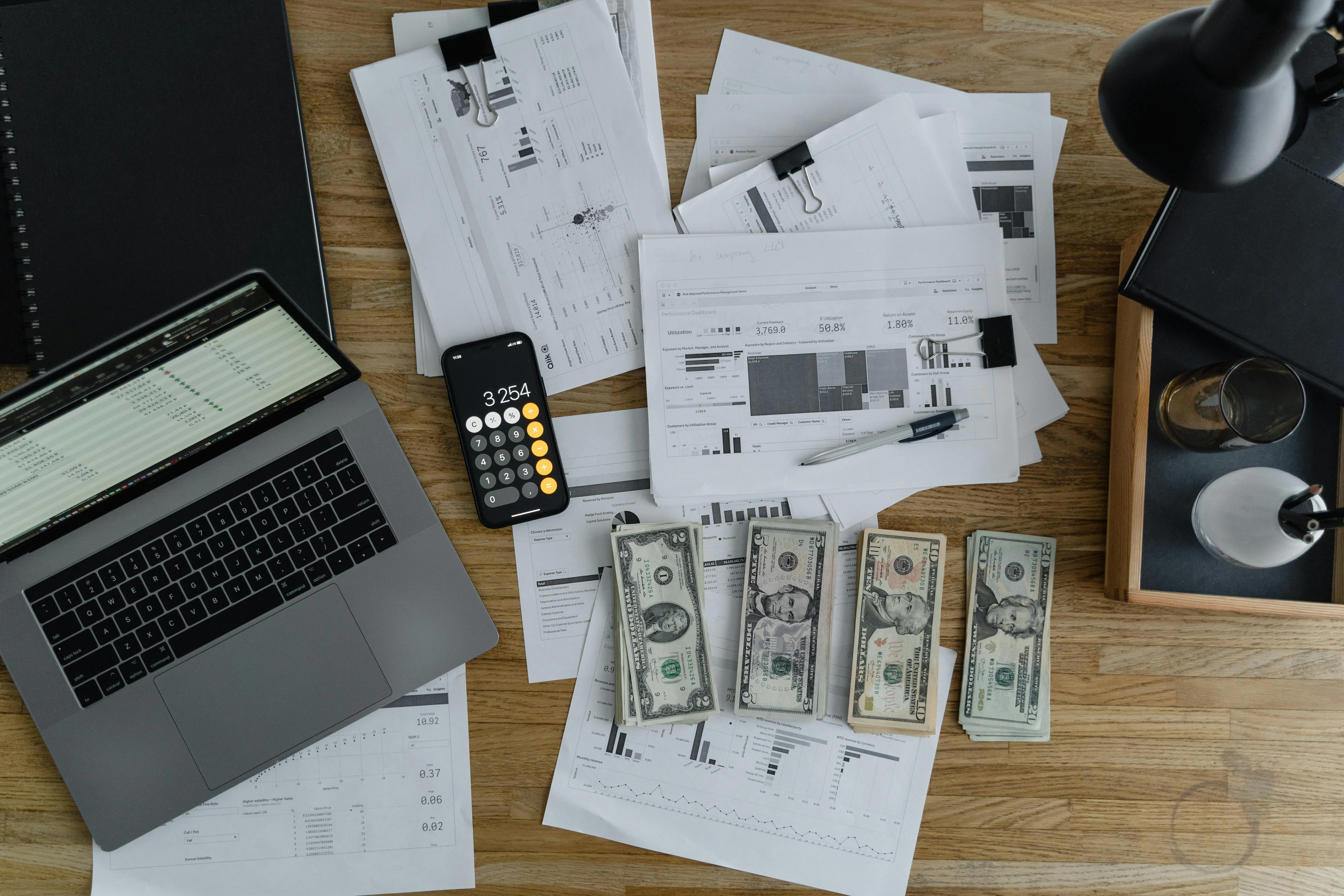 Desk with laptop, calculator app, and cash stacks.