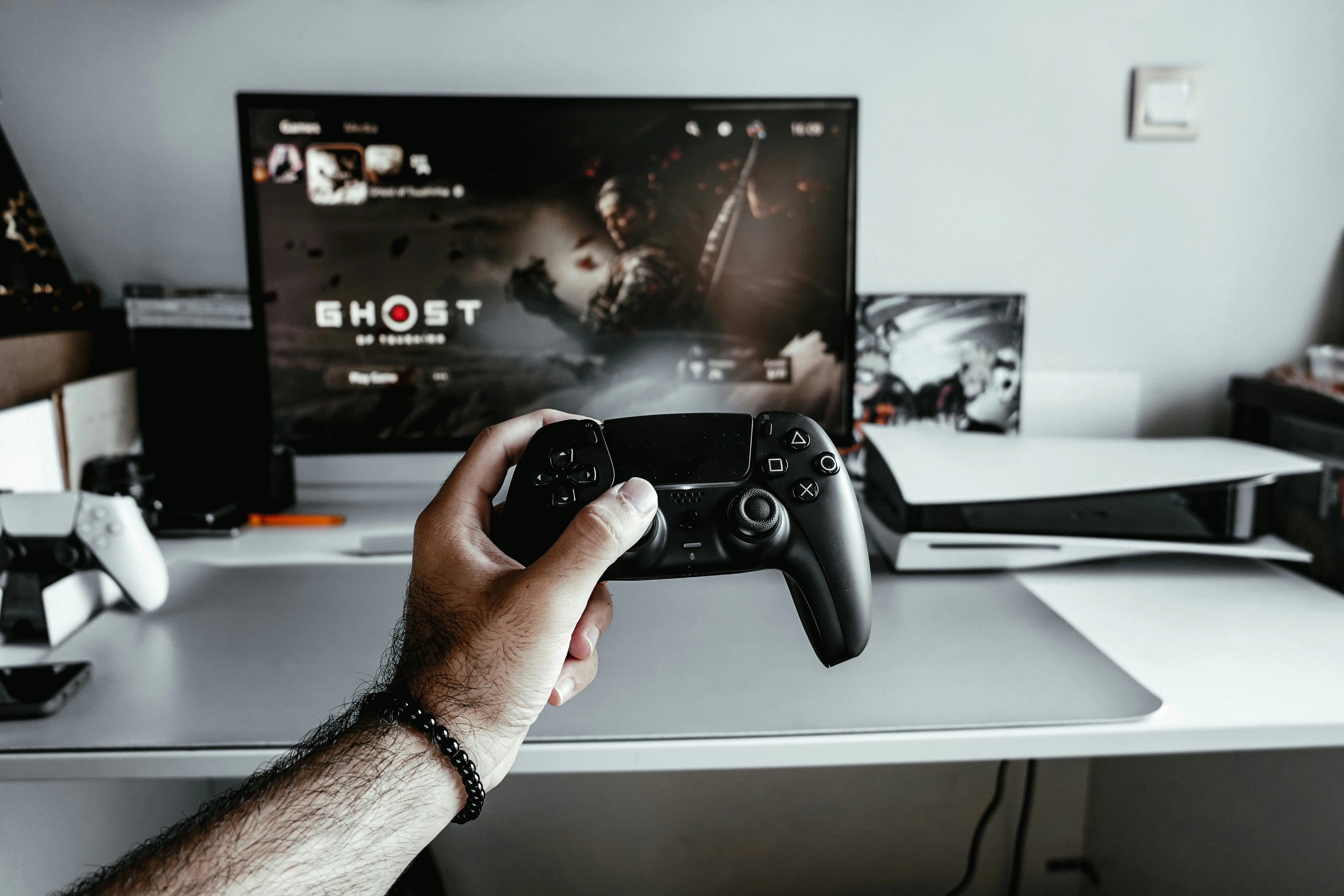 Hand holding controller, 'Ghost of Tsushima' on screen.