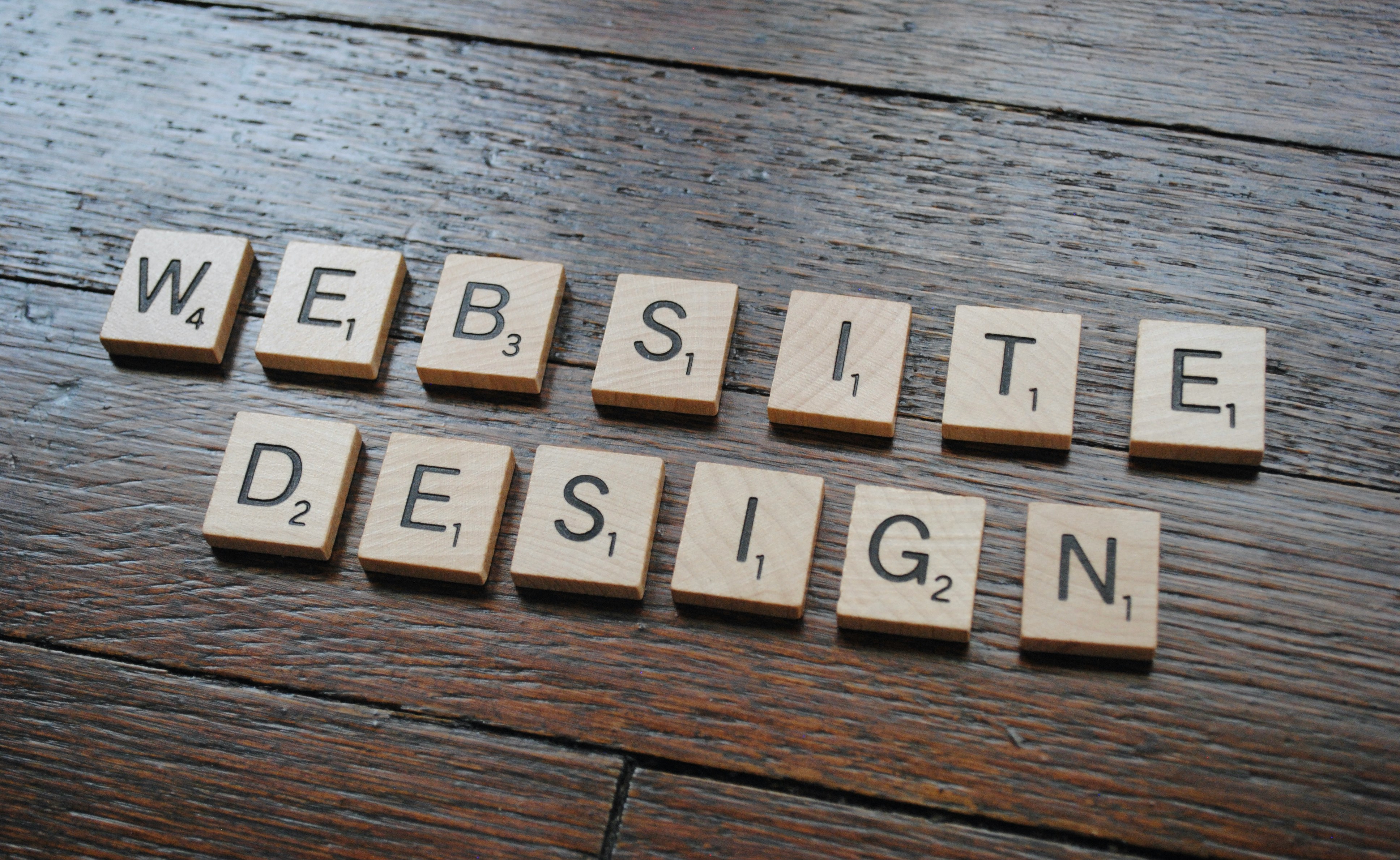 Scrabble tiles spelling 'WEBSITE DESIGN' on a wooden surface.