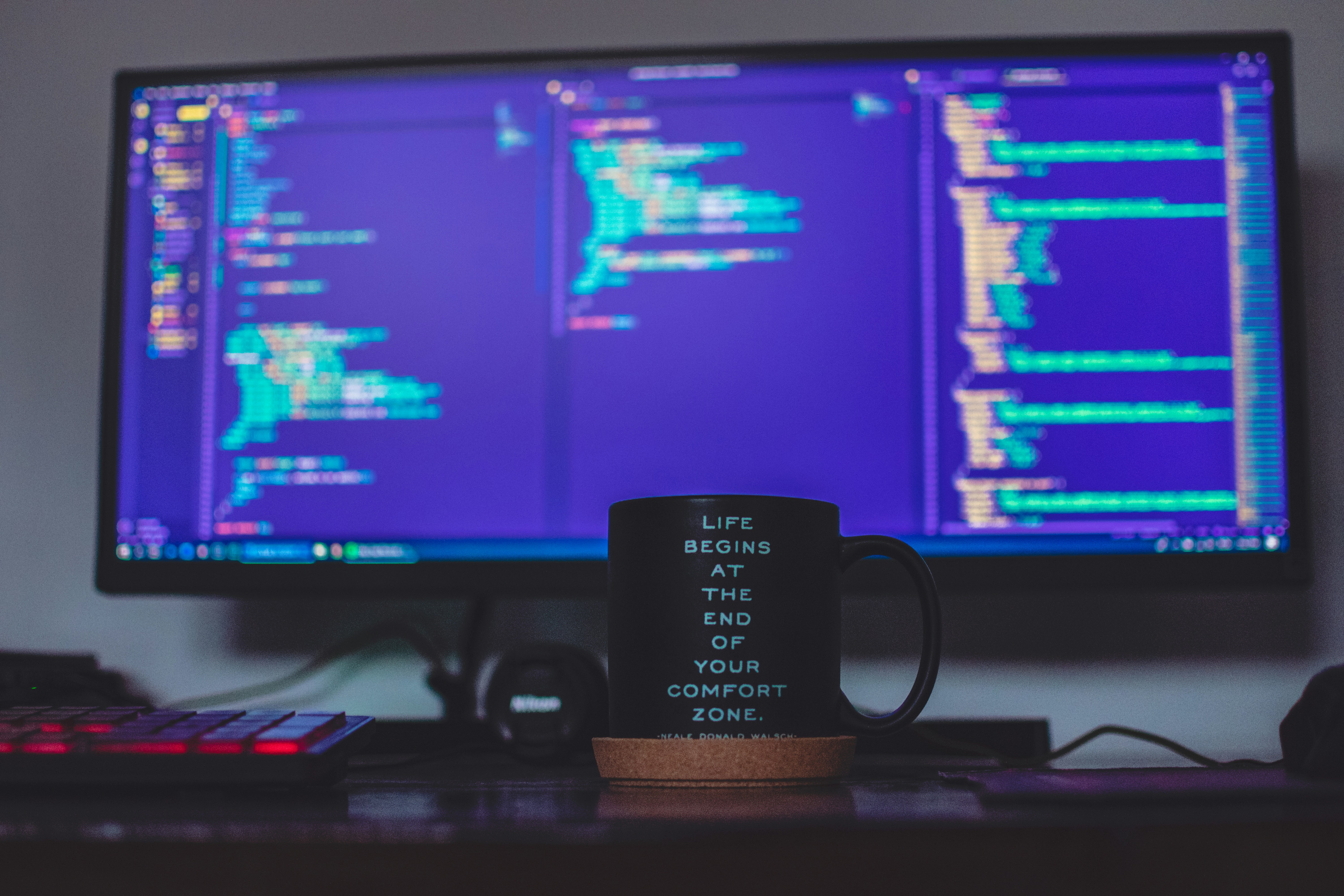 Coffee mug in front of code on dual monitors.