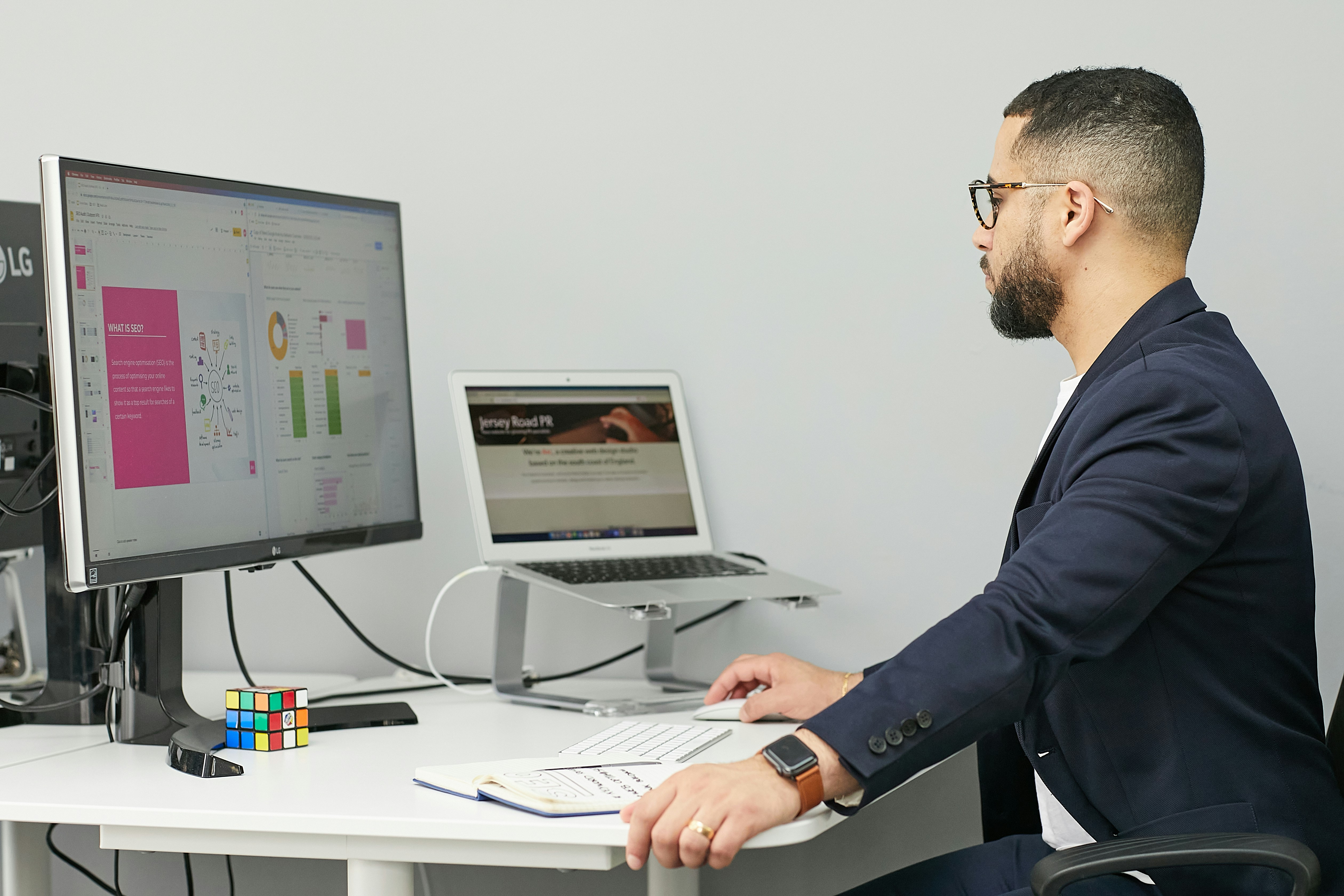 Person working on content with dual monitors and a notebook.